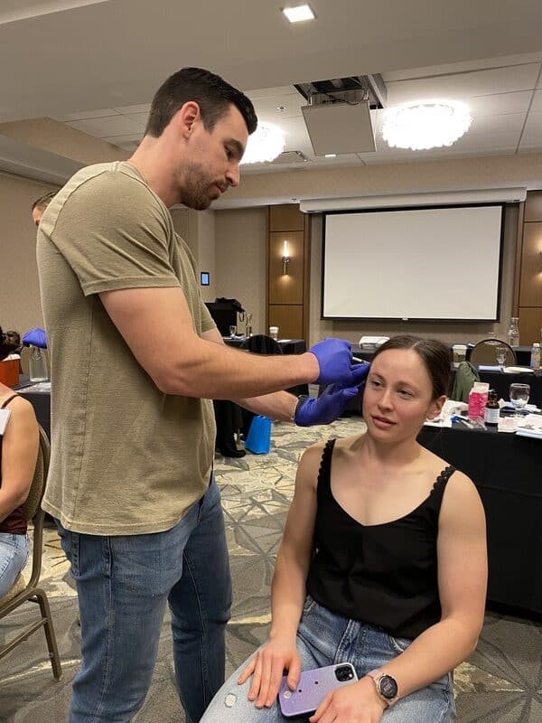 Clinician Practicing A Facial Injection Technique On A Seated Model During An Aafe Hands-On Tmj Training Course.
